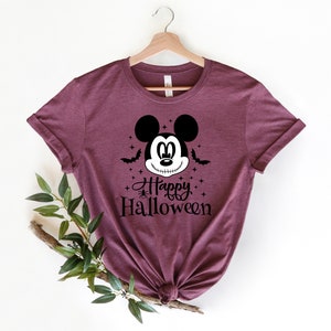 Puede incluir: Una camiseta color granate con un gr&aacute;fico en blanco y negro de Mickey Mouse con una sonrisa cosida. El texto "Happy Halloween" est&aacute; impreso debajo del gr&aacute;fico.