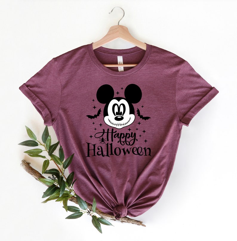 Puede incluir: Una camiseta color granate con un gr&aacute;fico en blanco y negro de Mickey Mouse con una sonrisa cosida. El texto "Happy Halloween" est&aacute; impreso debajo del gr&aacute;fico.
