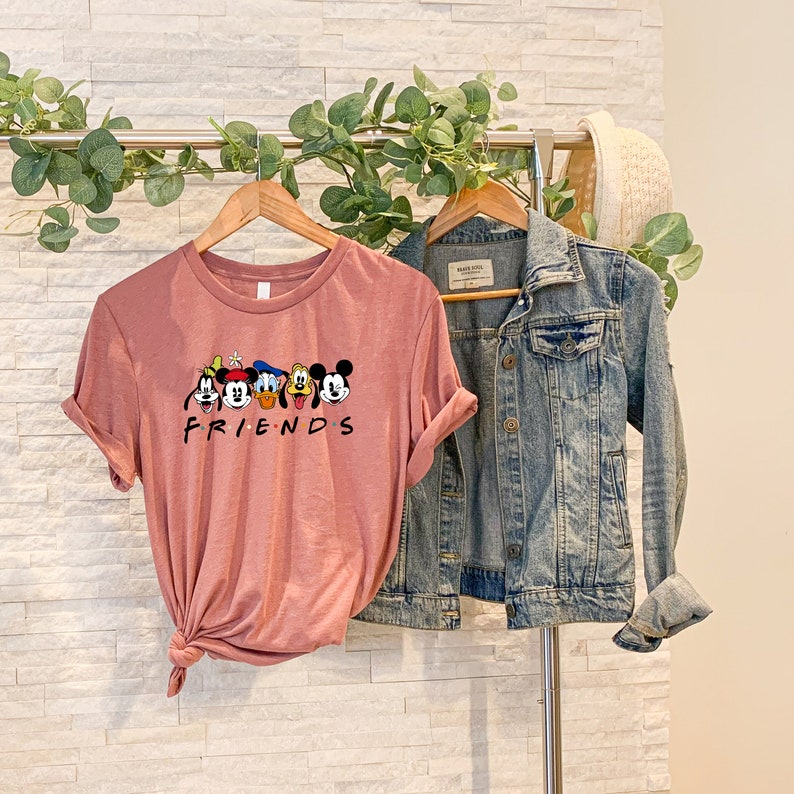 May include: A pink t-shirt with a graphic of Mickey Mouse and his friends. The shirt says "FRIENDS" underneath the graphic.