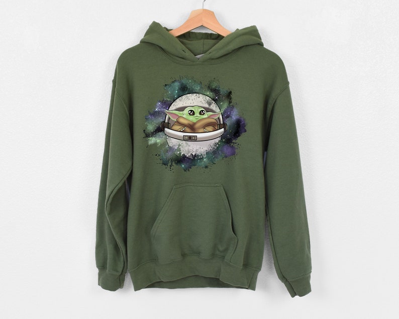 May include: A green hooded sweatshirt with a graphic print of a cartoon character in a spaceship against a galaxy background.