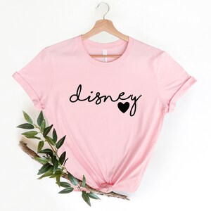 May include: Pink t-shirt with the word "disney" in black script with a small black heart next to it.