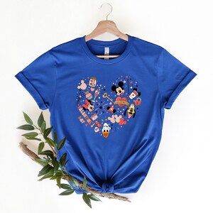 Pode incluir: Uma camiseta azul royal com um design em forma de cora&ccedil;&atilde;o que apresenta Mickey Mouse, Minnie Mouse e Donald Duck. O design inclui cora&ccedil;&otilde;es, estrelas e o texto "Valentine's Day".