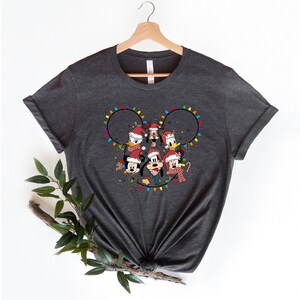 May include: A dark gray t-shirt with a Christmas-themed design featuring Mickey Mouse and his friends. The design shows Mickey Mouse, Minnie Mouse, Donald Duck, Goofy, and Pluto wearing Santa hats and surrounded by colorful Christmas lights in the shape of Mickey Mouse's ears.
