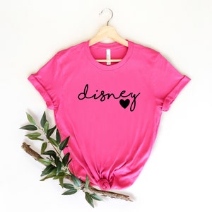 May include: Pink t-shirt with the word "disney" in black script with a small black heart next to it.
