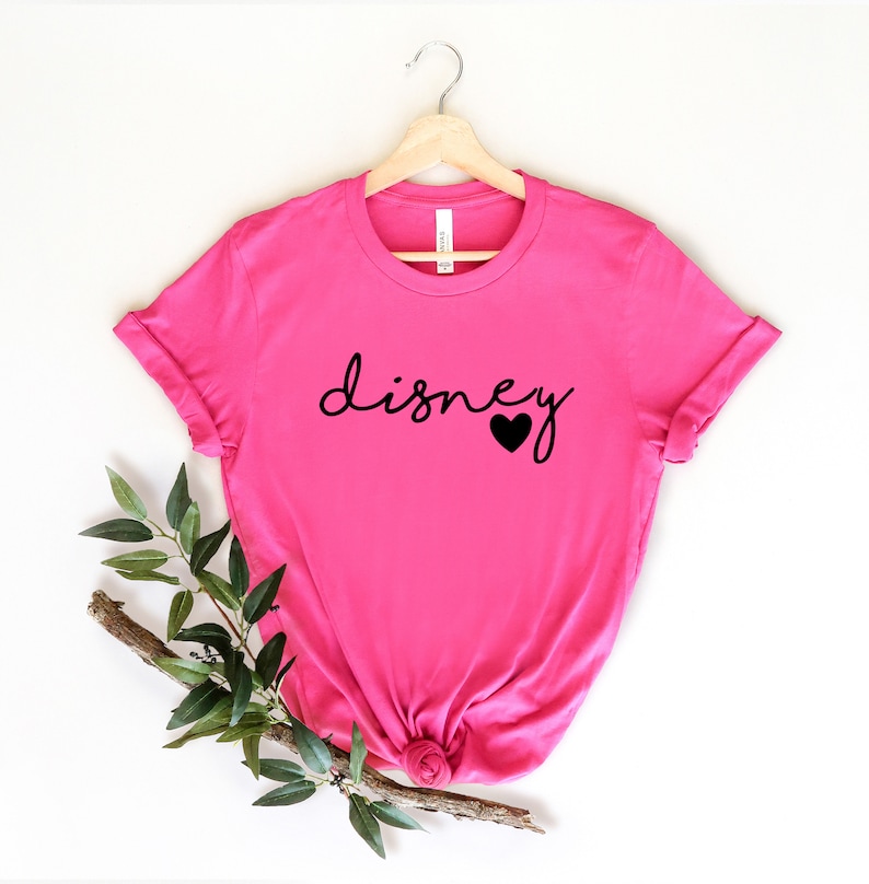 May include: Pink t-shirt with the word "disney" in black script with a small black heart next to it.