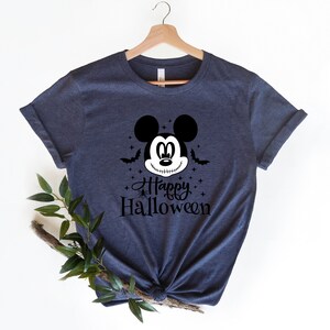 Puede incluir: Una camiseta azul marino con un gr&aacute;fico en blanco y negro de Mickey Mouse con una sonrisa cosida. El gr&aacute;fico tambi&eacute;n incluye murci&eacute;lagos, estrellas y el texto "Happy Halloween".