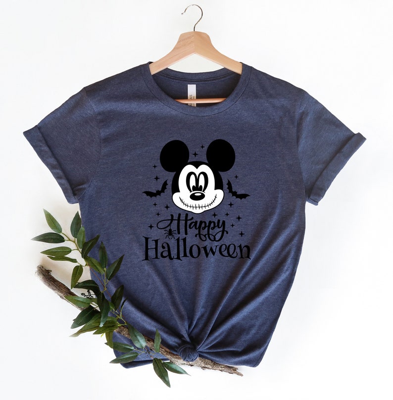 Puede incluir: Una camiseta azul marino con un gr&aacute;fico en blanco y negro de Mickey Mouse con una sonrisa cosida. El gr&aacute;fico tambi&eacute;n incluye murci&eacute;lagos, estrellas y el texto "Happy Halloween".