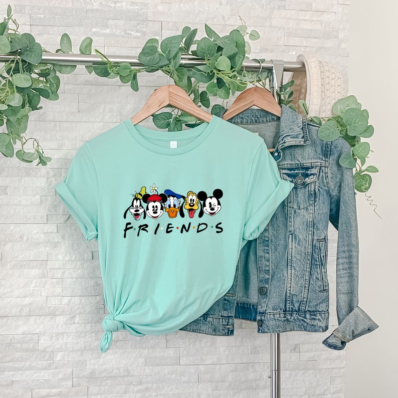 May include: A light blue t-shirt with a graphic of Mickey Mouse and his friends. The text "FRIENDS" is printed below the graphic.