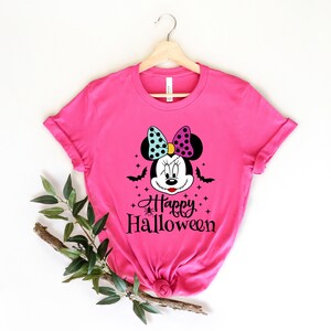 Puede incluir: Camiseta rosa con una ilustraci&oacute;n en blanco y negro de un rat&oacute;n de dibujos animados con una sonrisa cosida, que lleva un lazo azul y morado. El texto "Happy Halloween" est&aacute; impreso debajo del rat&oacute;n.