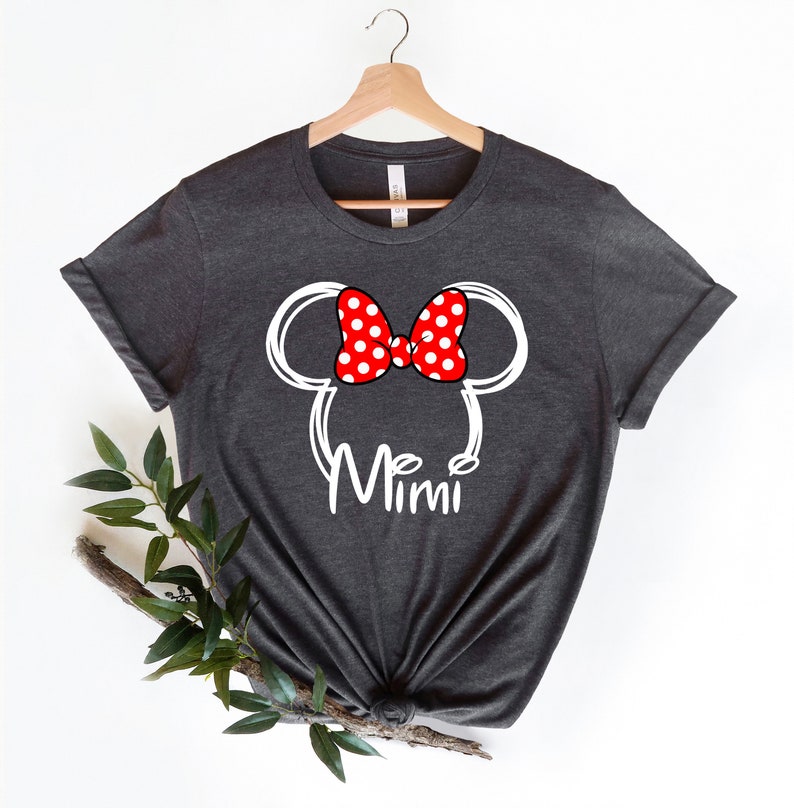 Op de afbeelding: Een donkergrijs T-shirt met een witte omtrek van Mickey Mouse oren en een rode strik met witte stippen. De tekst "Mimi" is onder de oren gedrukt.