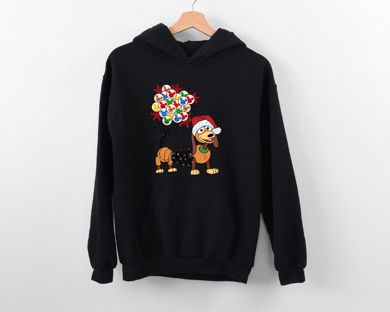 Pu&ograve; includere: Felpa con cappuccio nera con un cane dei cartoni animati che indossa un cappello da Babbo Natale e tiene delle luci natalizie. Il cane tiene anche un gruppo di ornamenti colorati. Un capo d'abbigliamento festivo a tema natalizio.