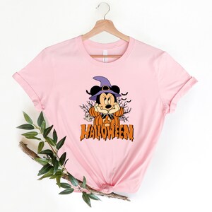 K&ouml;nnte beinhalten: Rosa T-Shirt mit einem Aufdruck von Mickey Mouse als Hexe f&uuml;r Halloween. Der Aufdruck enth&auml;lt einen K&uuml;rbis, Flederm&auml;use und das Wort "HALLOWEEN".