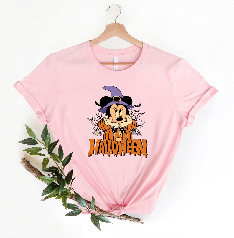 K&ouml;nnte beinhalten: Rosa T-Shirt mit einem Aufdruck von Mickey Mouse als Hexe f&uuml;r Halloween. Der Aufdruck enth&auml;lt einen K&uuml;rbis, Flederm&auml;use und das Wort "HALLOWEEN".