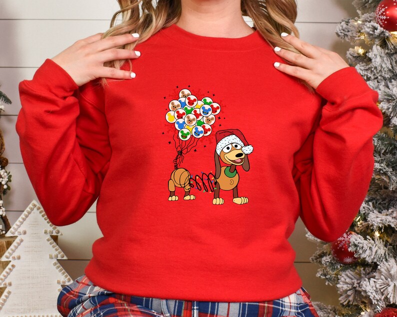 Pu&ograve; includere: Una felpa rossa con un bassotto dei cartoni animati con un cappello da Babbo Natale. Il bassotto tiene in mano dei palloncini con le facce di Topolino. La felpa &egrave; un design festivo natalizio.