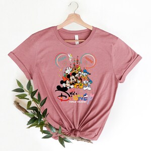 Puede incluir: Una camiseta rosa con un gr&aacute;fico de Mickey Mouse y sus amigos frente al Castillo de Cenicienta. El texto "Disney Family Vacation" est&aacute; debajo del gr&aacute;fico. El a&ntilde;o "2024" y la palabra "NAME" est&aacute;n en burbujas de di&aacute;logo sobre el castillo.