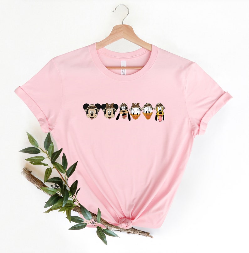 May include: Pink t-shirt with a line of Disney characters wearing safari hats. The characters are Mickey Mouse, Minnie Mouse, Goofy, Donald Duck, and Pluto.