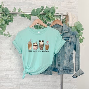 May include: A turquoise blue t-shirt with a graphic of four different coffee drinks. The text "Here for the drinks" is printed below the drinks.