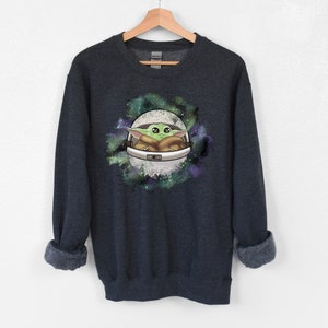 May include: Dark blue sweatshirt with a green alien character in a white space helmet against a galaxy background.