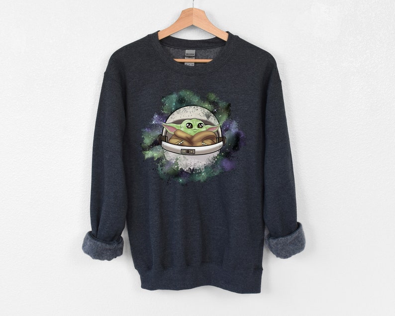 May include: Dark blue sweatshirt with a green alien character in a white space helmet against a galaxy background.