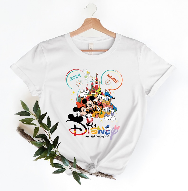 Puede incluir: Camiseta blanca con un dise&ntilde;o colorido de vacaciones familiares de Disney. El dise&ntilde;o presenta a Mickey Mouse, Minnie Mouse, Donald Duck, Goofy y Pluto frente al Castillo de Cenicienta. El texto "2024" y "NAME" est&aacute;n en las esquinas superiores del dise&ntilde;o. El texto "Disney Family Vacation" est&aacute; en la parte inferior del dise&ntilde;o.