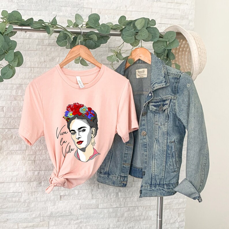 May include: A pink t-shirt with a graphic of Frida Kahlo wearing a flower crown and the text "Viva la Vida".