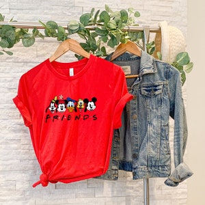 May include: Red t-shirt with a graphic of Mickey Mouse and his friends, including Donald Duck, Goofy, Pluto, and a cartoon flower. The text "FRIENDS" is printed below the characters.