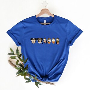 May include: A royal blue t-shirt with a line of Disney characters wearing safari hats. The characters are Mickey Mouse, Minnie Mouse, Pluto, Donald Duck, and Goofy.