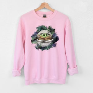 May include: Pink sweatshirt with a green and brown cartoon character in a spaceship surrounded by a galaxy print.