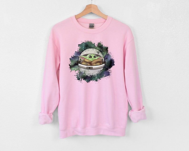 May include: Pink sweatshirt with a green and brown cartoon character in a spaceship surrounded by a galaxy print.