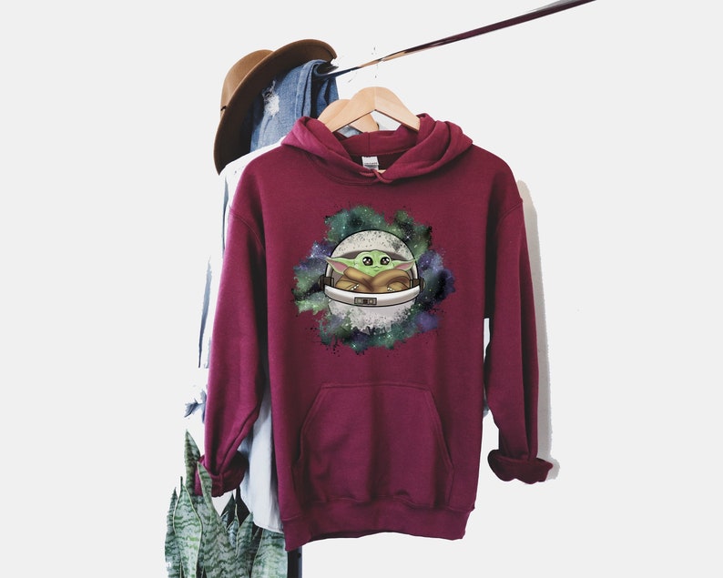 May include: Burgundy hooded sweatshirt with a graphic print of a green alien character in a spaceship against a galaxy background.
