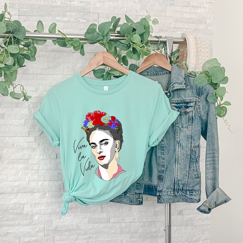 May include: A light blue t-shirt with a graphic of Frida Kahlo wearing a flower crown and the text "Viva la Vida".