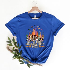 May include: A royal blue t-shirt featuring a colourful graphic of Mickey Mouse and his friends in front of a castle. The text "Not So Scary Halloween Party! 2023" is printed on the shirt.