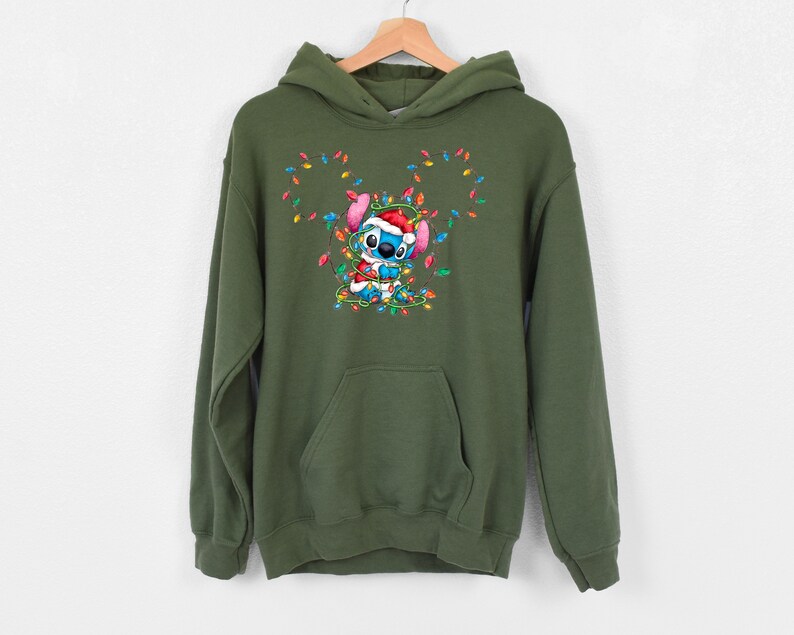 Może przedstawiać: Zielona bluza z kapturem z postacią z kresk&oacute;wki w czapce Świętego Mikołaja, otoczoną kolorowymi światełkami choinkowymi.