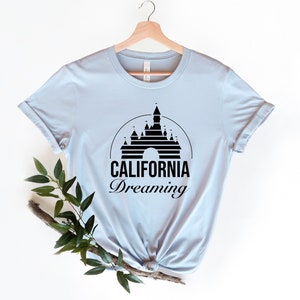 Puede incluir: Camiseta azul claro con una silueta negra del Castillo de la Bella Durmiente y el texto "CALIFORNIA Dreaming".