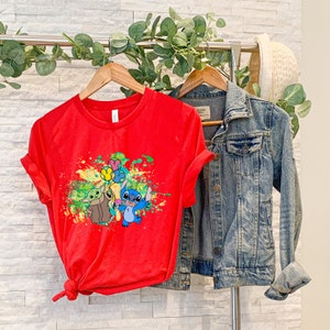 K&ouml;nnte beinhalten: Rotes T-Shirt mit einem bunten Spritzlack-Design mit Stitch und Baby Yoda, die Ballons halten.