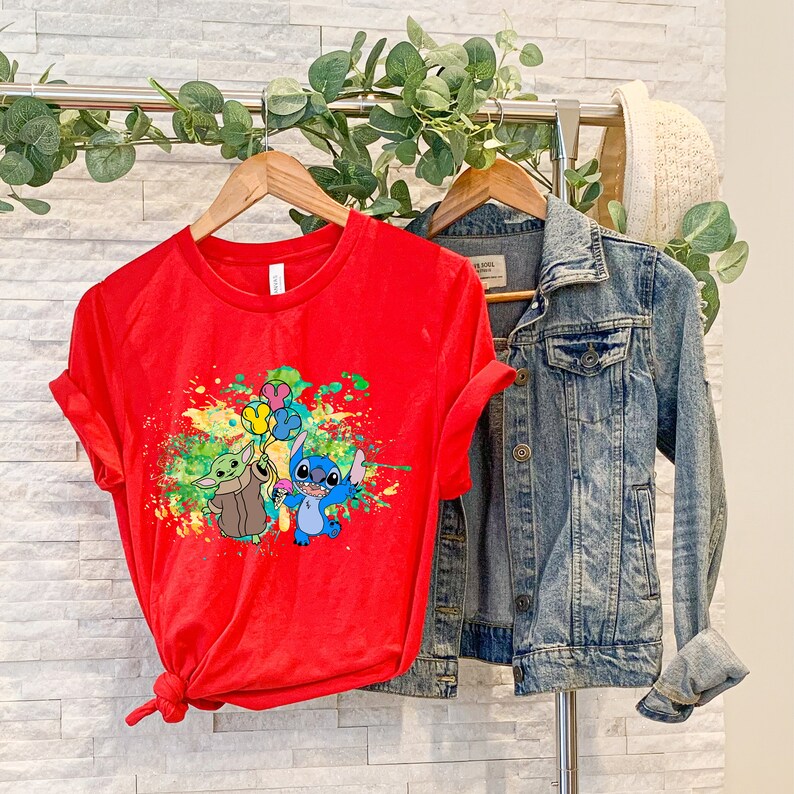 K&ouml;nnte beinhalten: Rotes T-Shirt mit einem bunten Spritzlack-Design mit Stitch und Baby Yoda, die Ballons halten.