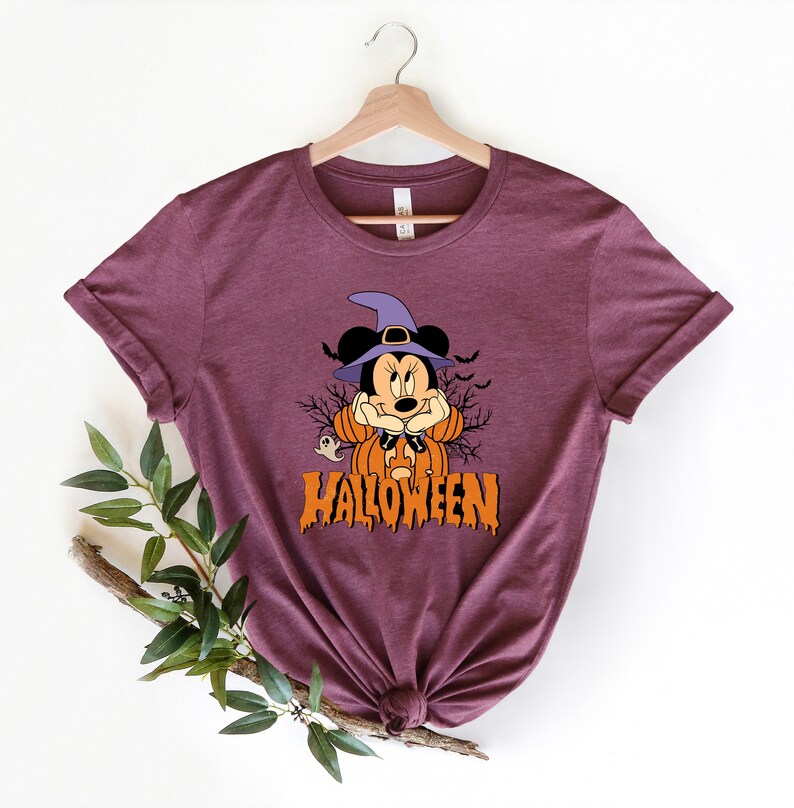 K&ouml;nnte beinhalten: Ein maroonfarbenes T-Shirt mit einem Aufdruck von Mickey Mouse als Hexe mit einem K&uuml;rbis und dem Text "HALLOWEEN".