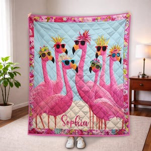 May include: A pink flamingo quilt featuring six flamingos wearing sunglasses and decorative headwear. The quilt has a light blue background with a diamond pattern and a floral border. The name "Sophia" is written on the quilt.