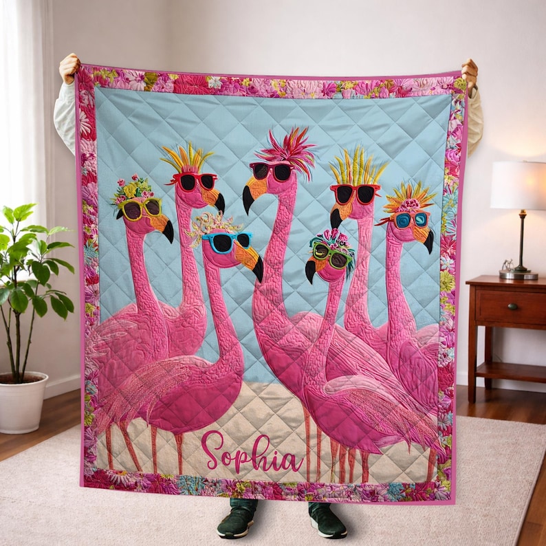 May include: A pink flamingo quilt featuring six flamingos wearing sunglasses and decorative headwear. The quilt has a light blue background with a diamond pattern and a floral border. The name "Sophia" is written at the bottom.