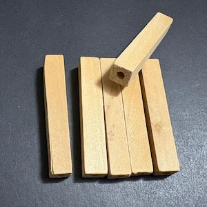 Può includere: Una collezione di sei porta incenso rettangolari in legno. Cinque sono allineati, mentre uno è angolato, rivelando un foro praticato. I supporti sono di colore marrone chiaro.