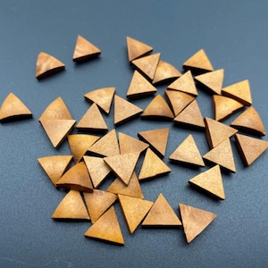 Könnte beinhalten: Eine Ansammlung kleiner Holz-Dreiecke, die auf einer dunklen Oberfläche verstreut sind. Die Dreiecke haben eine warme, hellbraune Farbe und jede hat drei Seiten. Die Formen sind gleichmäßig, was darauf hindeutet, dass sie Bestandteile eines größeren Objekts oder Spiels sind.