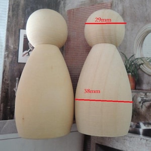 May include: Two unfinished wooden peg dolls. The head measures 2.9cm across, and the body is 3.8cm wide. The dolls are light beige in colour and have a smooth, rounded shape, perfect for crafting or decoration.