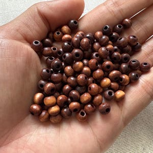 May include: A handful of small, round wooden beads in varying shades of brown, from light tan to dark chocolate. Each bead has a hole through the center, suggesting they are for stringing. The beads are smooth and appear to be natural wood.