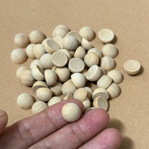 Op de afbeelding: Een verzameling kleine, onafgewerkte houten halve ronde bollen. Sommige bollen zijn heel, terwijl andere gehalveerd zijn en een holle binnenkant onthullen. De bollen zijn lichtbeige van kleur en lijken van natuurlijk hout te zijn.