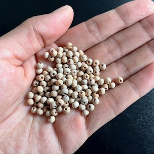 Könnte beinhalten: Eine Handvoll kleiner, hellfarbiger Holzperlen mit Löchern. Die Perlen haben einen natürlichen, neutralen Farbton und scheinen in Größe und Form einheitlich zu sein. Sie werden in einer offenen Hand gehalten, was auf Bastel- oder Schmuckzwecke hindeutet.