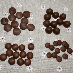 May include: A collection of small, round, dark brown wooden discs arranged in groups on a light beige fabric decorated with white and red floral patterns. The discs appear to be game pieces.