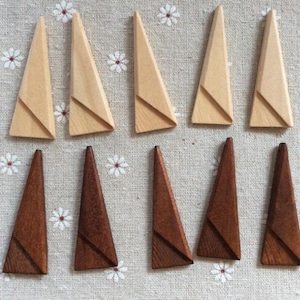 Puede incluir: Diez objetos de madera en forma de triángulo, cinco de color claro y cinco de color oscuro, dispuestos sobre una superficie con estampado floral. Cada triángulo tiene un elemento de diseño geométrico. Los objetos parecen hechos a mano.