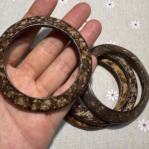 Puede incluir: Un conjunto de cuatro pulseras de color marr&oacute;n y beige. Las pulseras tienen un patr&oacute;n moteado y una forma suave y redondeada. Fabricadas con un material natural, son adecuadas para el uso diario. Las pulseras se muestran sobre un fondo floral.