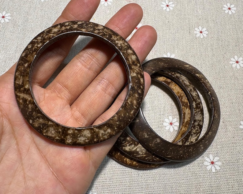 Puede incluir: Un conjunto de cuatro pulseras de color marr&oacute;n y beige. Las pulseras tienen un patr&oacute;n moteado y una forma suave y redondeada. Fabricadas con un material natural, son adecuadas para el uso diario. Las pulseras se muestran sobre un fondo floral.