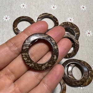 Puede incluir: Una colecci&oacute;n de anillos de madera circulares marrones con un patr&oacute;n natural y texturizado. Los anillos se sostienen en una mano, mostrando su tama&ntilde;o y dise&ntilde;o. Los anillos son probablemente para manualidades o decoraci&oacute;n del hogar.